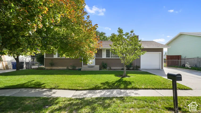 Single-level residence with a front lawn, mature trees, and an attached single-car garage