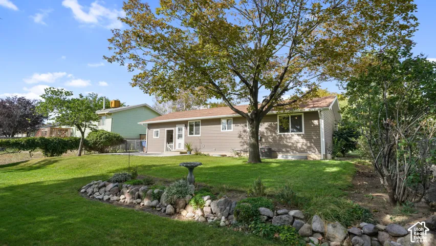 Expansive backyard featuring a manicured lawn, mature trees, and a decorative stone-lined garden bed