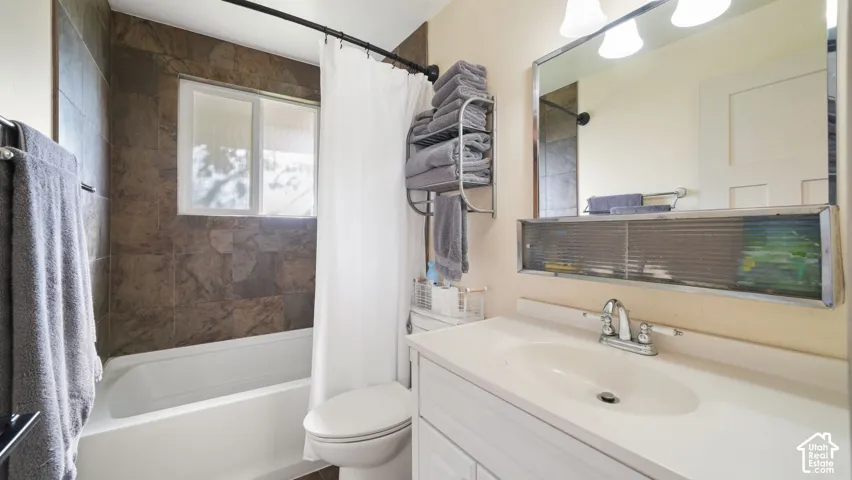 Bathroom featuring a white vanity with an integrated sink, a wall-mounted mirror with integrated lighting, a toilet, and a bathtub with tile surround