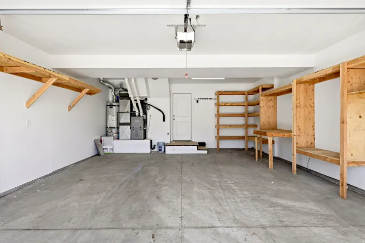 Attached garage with concrete flooring, built-in wooden shelving, overhead storage, and a utility area