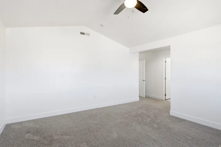 Vaulted ceiling with a ceiling fan, grey carpeting, white walls, and white interior doors
