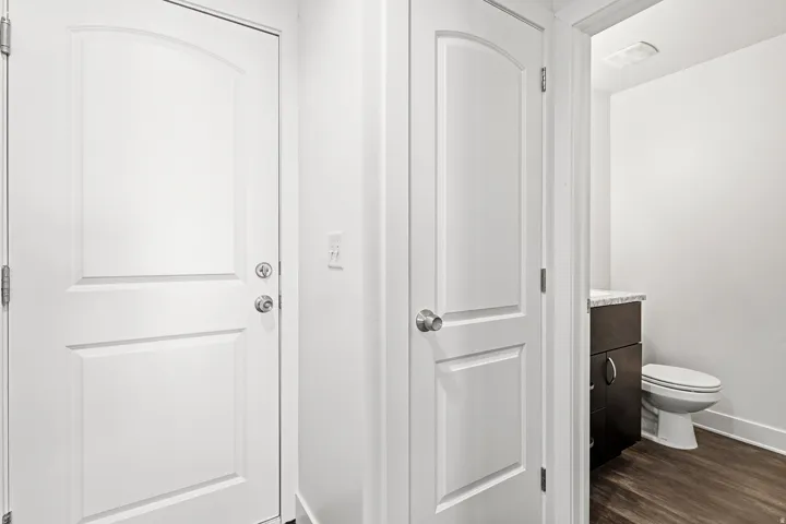 White interior doors, wood-finish flooring, dark wood-finish vanity with countertop, and a white toilet