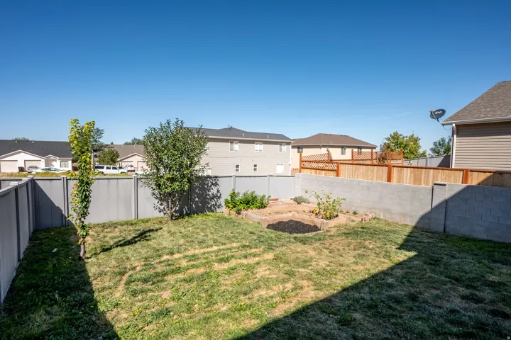 Fenced backyard featuring a raised garden bed, young trees, and a combination of gray panel and wood fencing