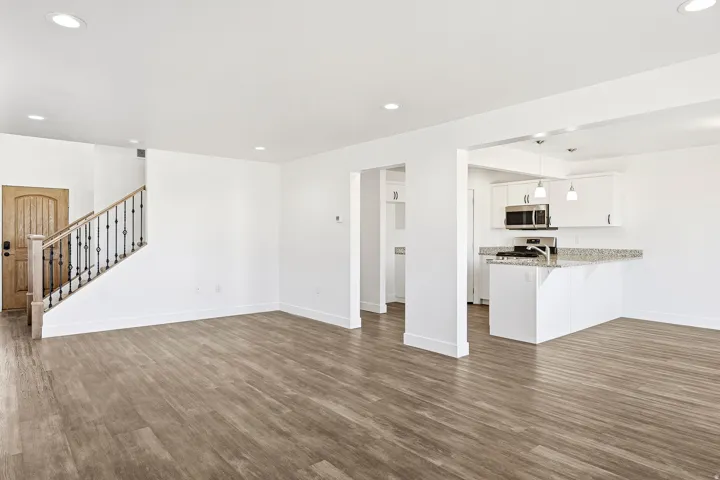 Wood-finish flooring, recessed lighting, and a kitchen featuring white cabinetry, stainless steel appliances, and a stone-finish countertop