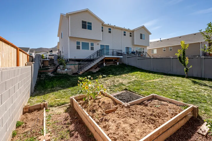 Expansive backyard featuring a manicured lawn, raised garden beds, a concrete block retaining wall, and a wood privacy fence