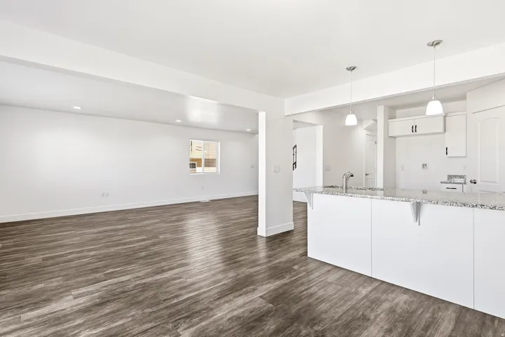 Open-concept living area featuring wood-finish flooring, recessed lighting, and a kitchen island with stone countertop and pendant lighting