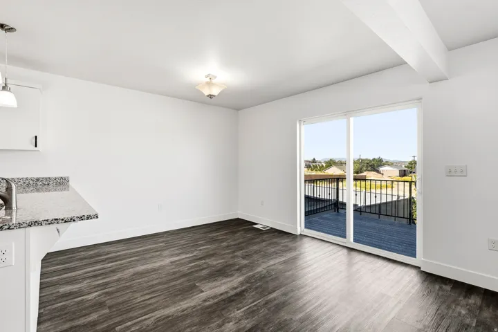 Wood-finish flooring, white walls, and a sliding glass door providing access to an outdoor deck with black railings