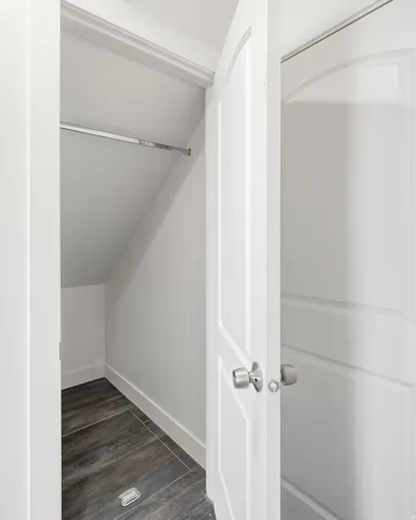Storage closet featuring a hanging rod and wood-finish flooring