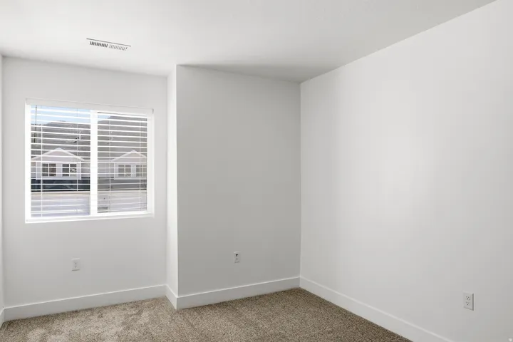 Neutral wall finishes, textured carpeting, and a window with horizontal blinds