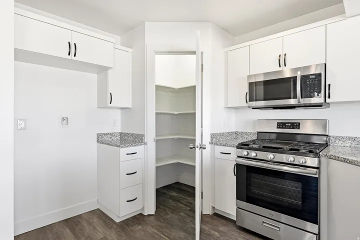 White cabinetry with black hardware, stainless steel gas range, built-in stainless steel microwave, granite countertops, and wood-finish flooring
