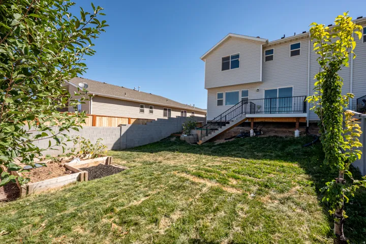 Rear exterior featuring a wooden deck with black metal railing, sliding glass door access, and an exterior staircase