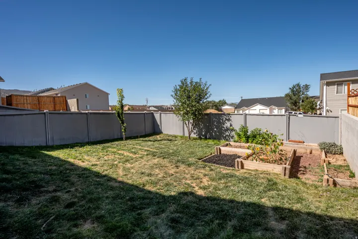 Expansive rear yard featuring a partial grass lawn, mature trees, and multiple raised garden beds