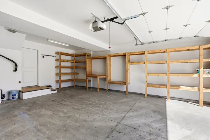 Concrete flooring with extensive built-in wooden shelving, a dedicated workbench area, and an automatic garage door opener