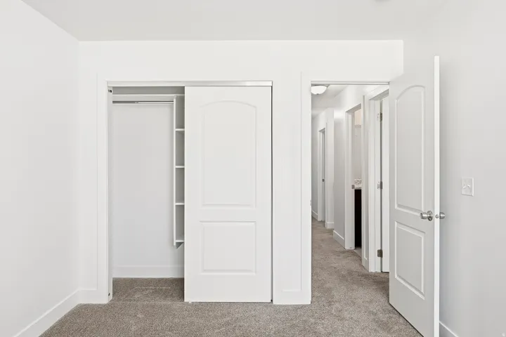 Carpeted flooring, white walls, built-in closet shelving, sliding closet doors, and interior arched panel doors