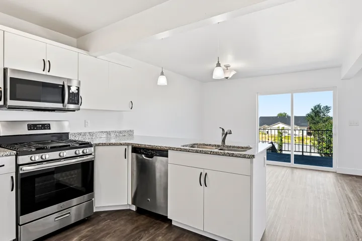 White shaker cabinetry, stainless steel appliances, speckled stone countertops, wood-finish flooring, and a sliding glass door