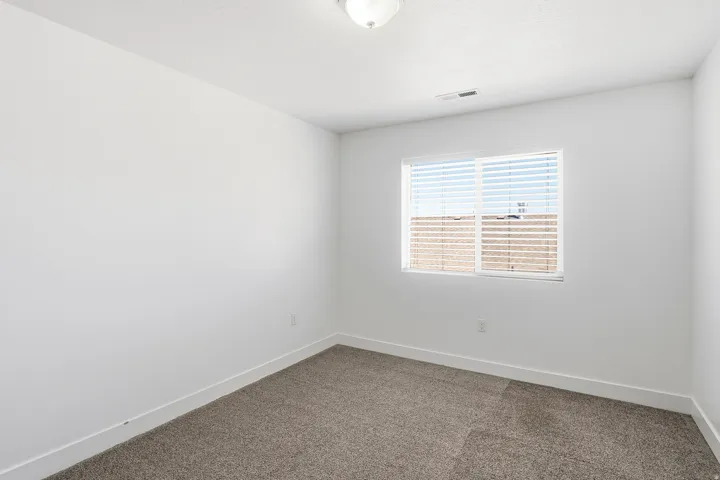 Carpeted room with a single window featuring blinds and a ceiling-mounted light fixture