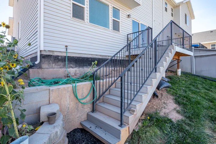 Exterior featuring light-colored horizontal siding, a multi-level deck with black metal railings, and a concrete block retaining wall