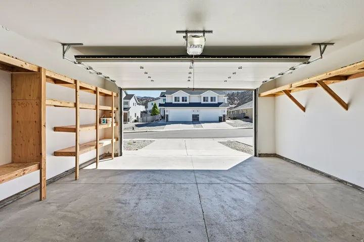 Spacious garage with a concrete floor, built-in wood shelving, an overhead garage door opener, and a white paneled garage door