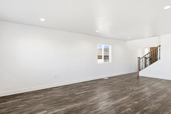 Recessed lighting, wood-finish flooring, white walls, and a staircase with wrought iron balusters and a wood handrail