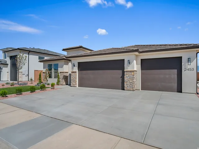 Stucco exterior with stone accents, two-car garage, concrete driveway, and front landscaping