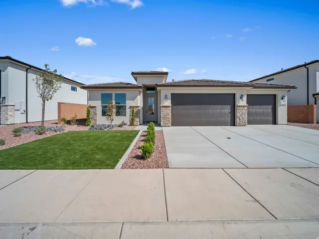 Stucco exterior with stone accents, a two-car garage, a single-car garage, manicured artificial turf, and desert landscaping