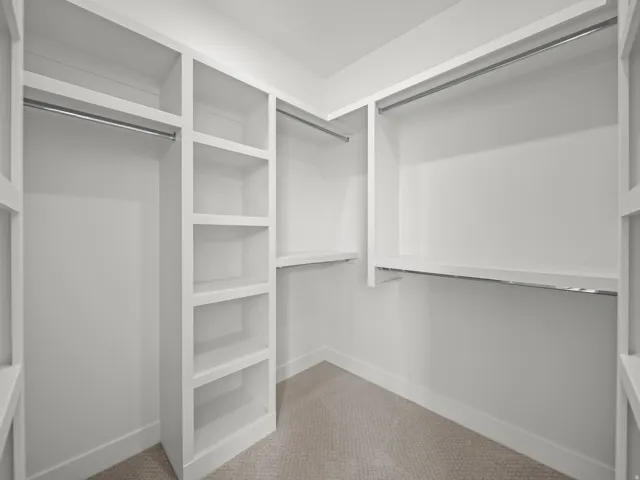 Custom closet system featuring built-in shelving, multiple hanging rods, and neutral carpeting