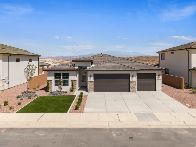 Contemporary stucco exterior with stone accents, a two-car garage, concrete driveway, and a landscaped front yard featuring turf and decorative rock