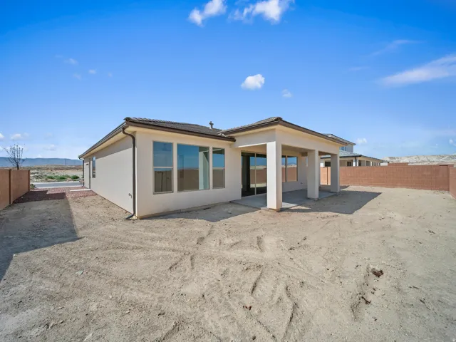 Stucco exterior with multiple windows, covered patio with concrete flooring, and a fenced backyard