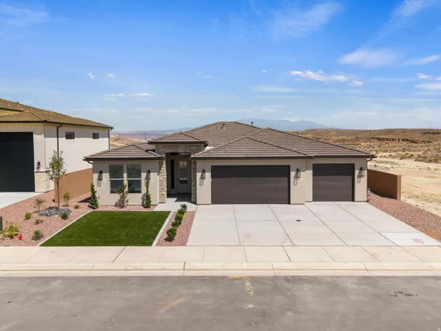 Contemporary stucco exterior with stone accents, a multi-car garage, concrete driveway, and low-maintenance landscaping