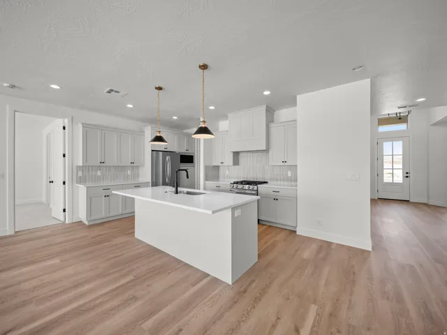 Kitchen with light wood-finish flooring, white cabinetry, a central island with a sink, stainless steel appliances, and pendant lighting