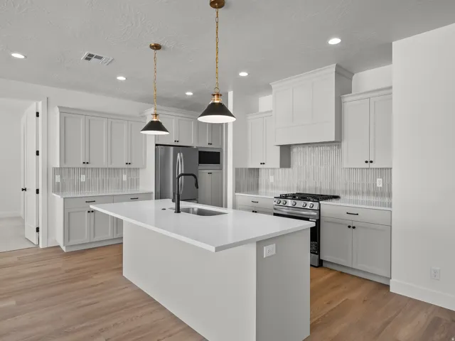 Kitchen featuring white cabinetry, light countertops, wood-finish flooring, stainless steel appliances, and a central island with a sink