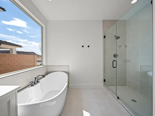 Freestanding soaking tub with dark-finish fixtures, a spacious walk-in shower with clear glass enclosure, and large format floor tiling