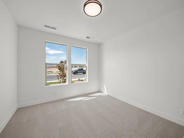 Bright, naturally lit bedroom featuring dual large windows with expansive sightlines, neutral textured carpet flooring, and ceiling-mounted light fixture