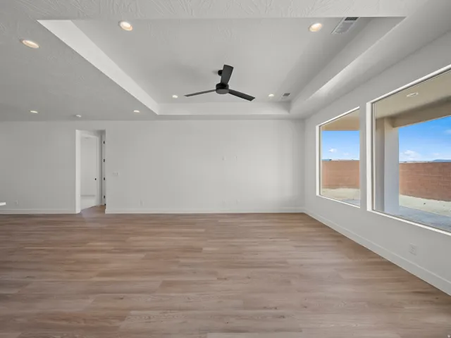 Tray ceiling with recessed lighting, modern ceiling fan, wood-finish flooring, and large windows