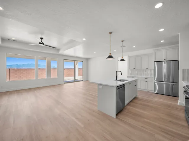 Open-concept kitchen and living area featuring wood-finish flooring, white cabinetry, a kitchen island with sink, and stainless steel appliances