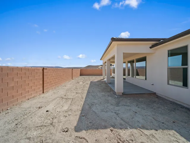 Expansive backyard with a stucco exterior, covered patio, large windows, and a block wall
