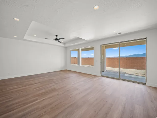 Wood-finish flooring throughout, tray ceiling with recessed lighting, ceiling fan, and large sliding glass door with two windows