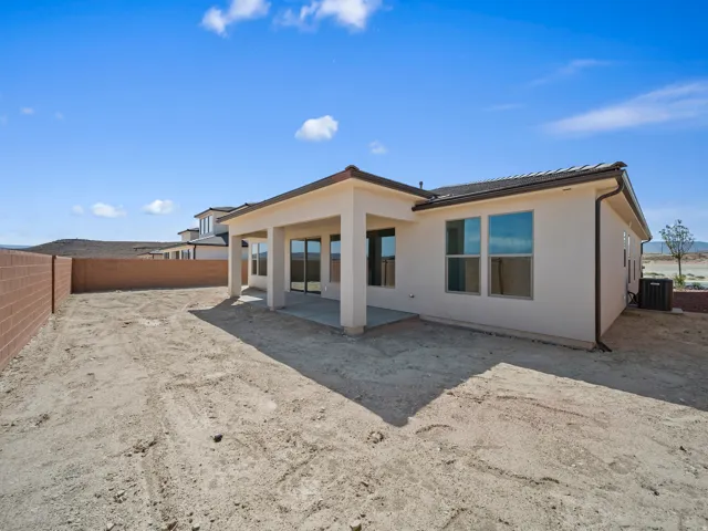 Rear exterior with stucco siding, covered patio, multiple windows, and a block fence