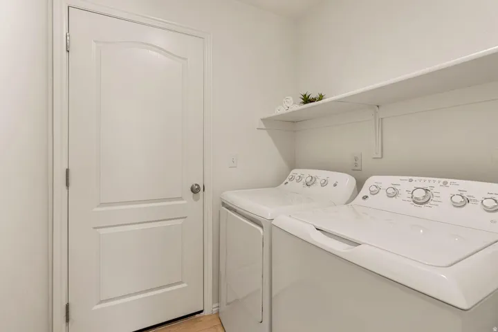 Laundry area with a white door featuring a rounded panel design, light-colored flooring, and an integrated wall shelf