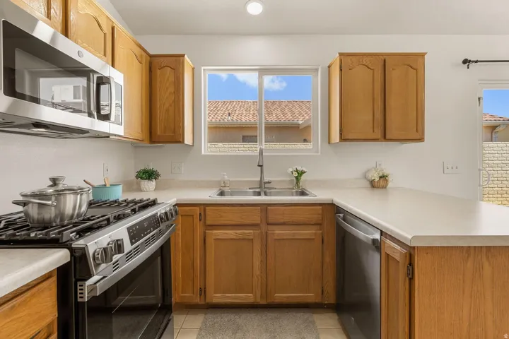 U-shaped kitchen featuring light wood cabinetry, a stainless steel gas range, stainless steel microwave, stainless steel dishwasher, and a double basin sink with a single-lever faucet