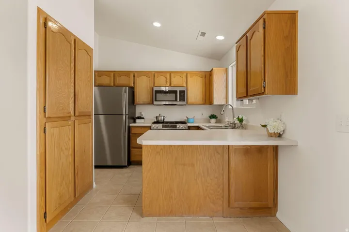 Kitchen featuring wood cabinetry, stainless steel appliances, a tile floor, and a vaulted ceiling