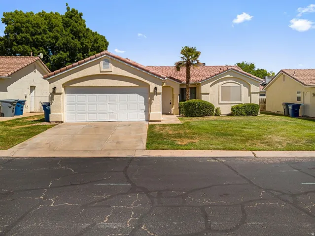 Stucco exterior with a tiled roof, attached garage, and manicured front lawn