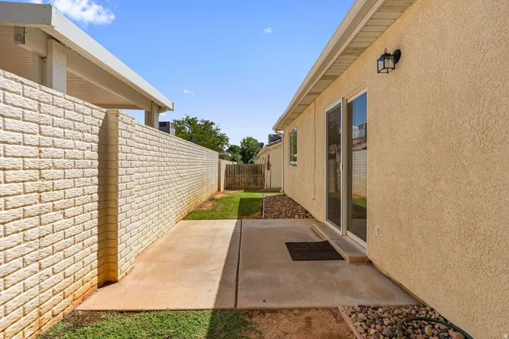 Stucco exterior with sliding glass door access to a concrete patio, bordered by a brick privacy wall and a gravel bed