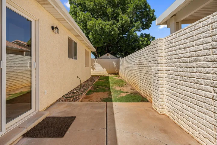 Exterior stucco finish, sliding glass door, paved concrete patio, brick privacy wall, and landscaped rock bed