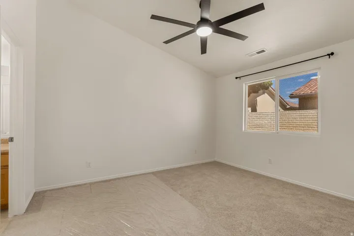 Vaulted ceiling featuring a ceiling fan with integrated lighting, window with a black curtain rod, neutral-toned carpeting, and white walls