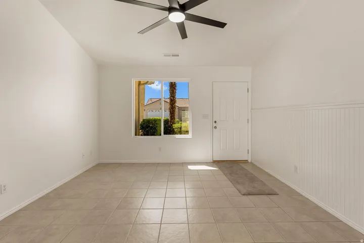 Tile flooring, white paneled wall, ceiling fan, white door, and a window providing natural light
