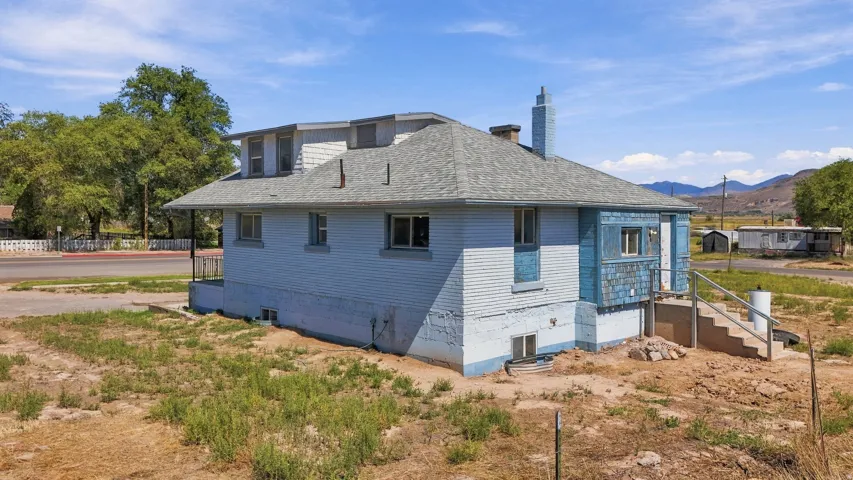 Two-story residence featuring dormer windows, a pitched roof, exterior stairs with railing, and a visible chimney