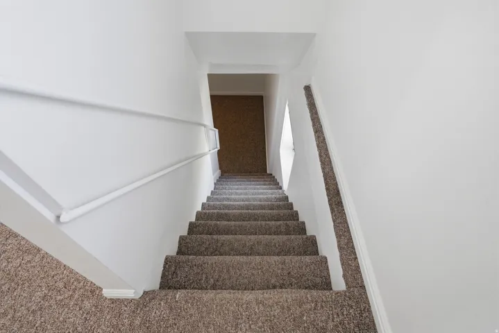 Staircase featuring neutral carpet flooring and a white handrail