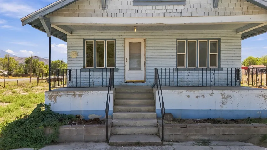 Front porch with concrete steps, black metal railings, and a brick facade