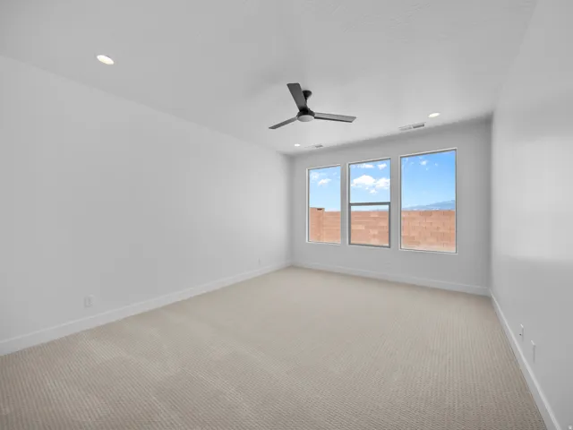 Spacious room featuring neutral carpeting, three large windows, a modern ceiling fan, and recessed lighting
